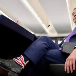 Nigel Farage sitting in a lounge chair, wearing union flag socks by J.M Executive