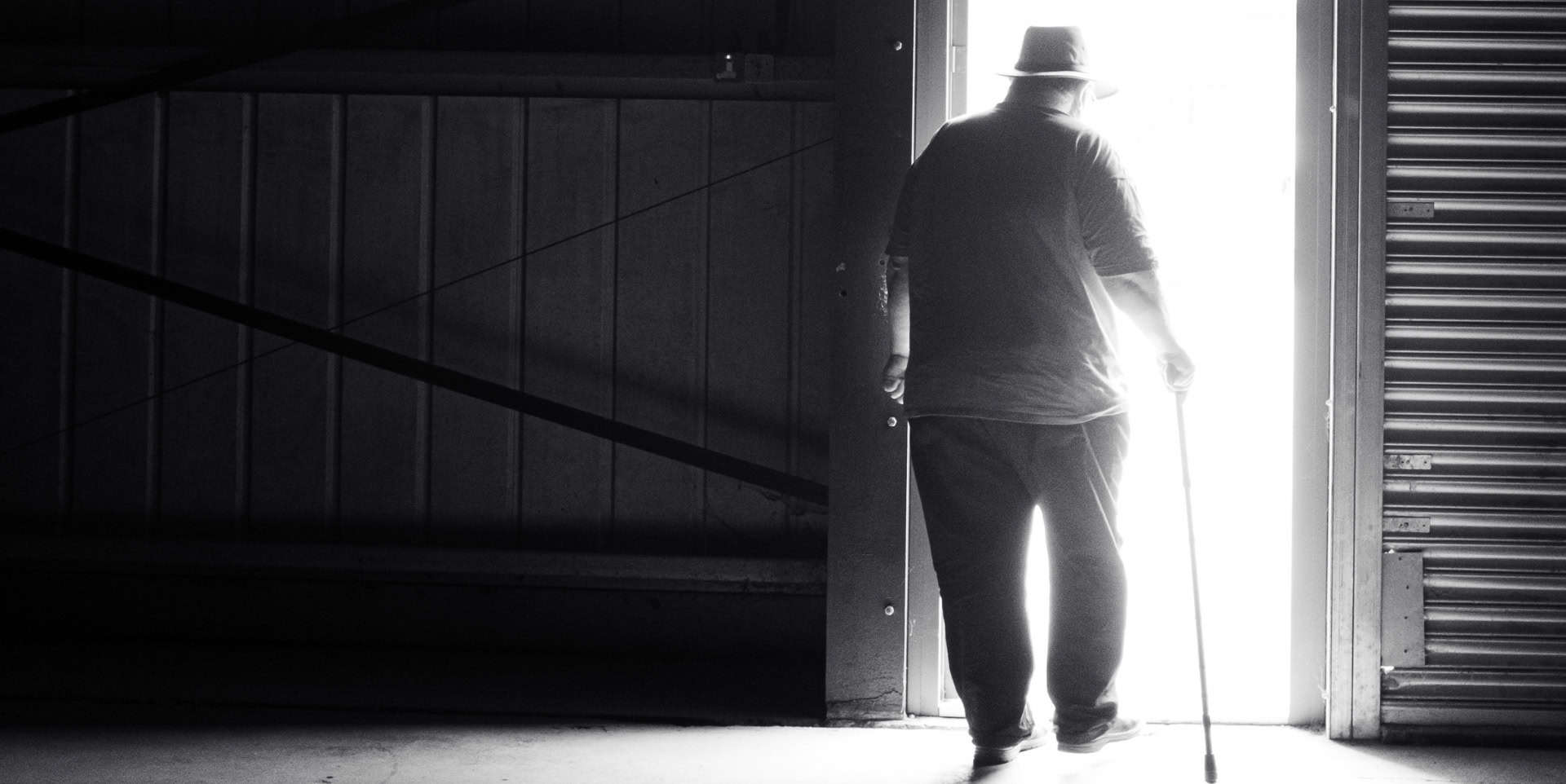 Older-man-with-walking stick walking through a light doorway