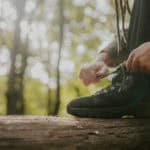 Person resting their foot on a tree trunk whilst they do up the laces of their walking boots