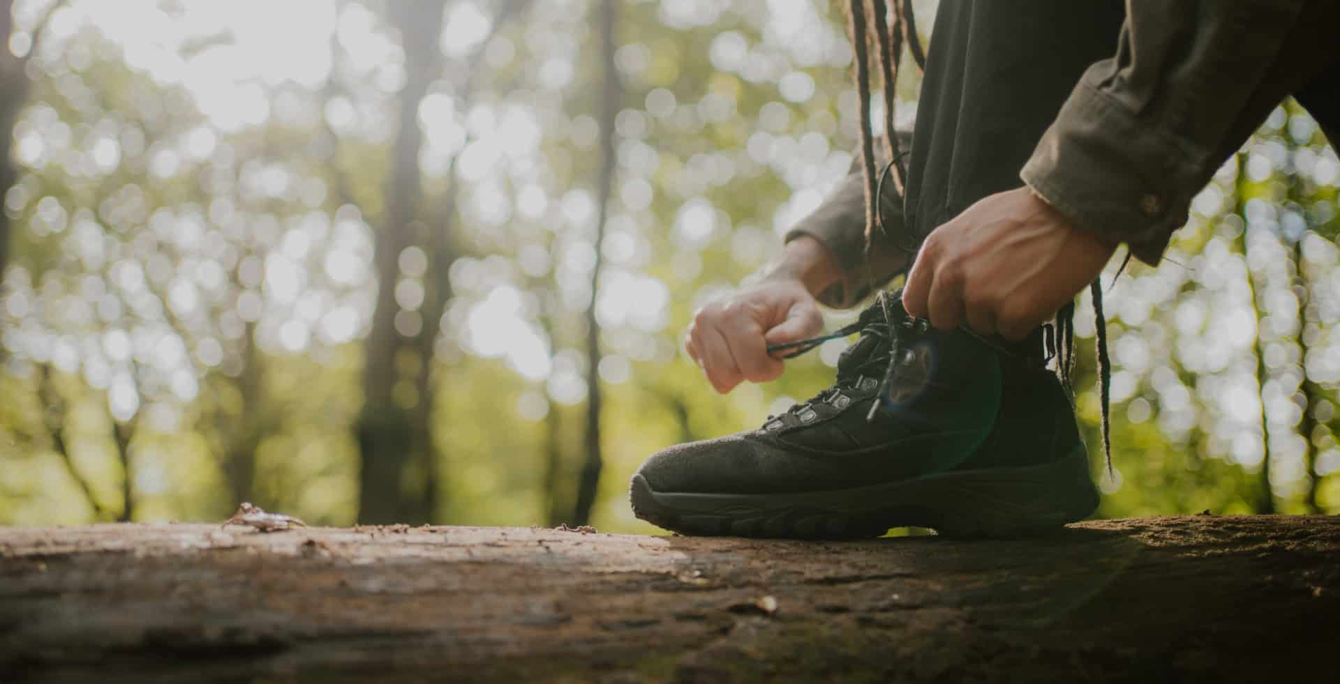 Person resting their foot on a tree trunk whilst they do up the laces of their walking boots