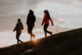 Three people walking down a hill at sunset