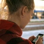 woman holding a mobile phone whilst standing on the street