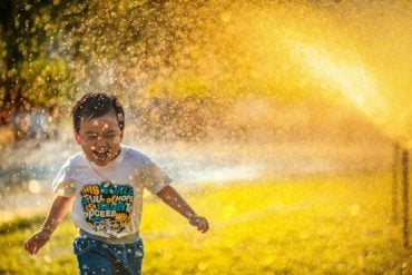 young boy running through a hose pipe spray in the sun