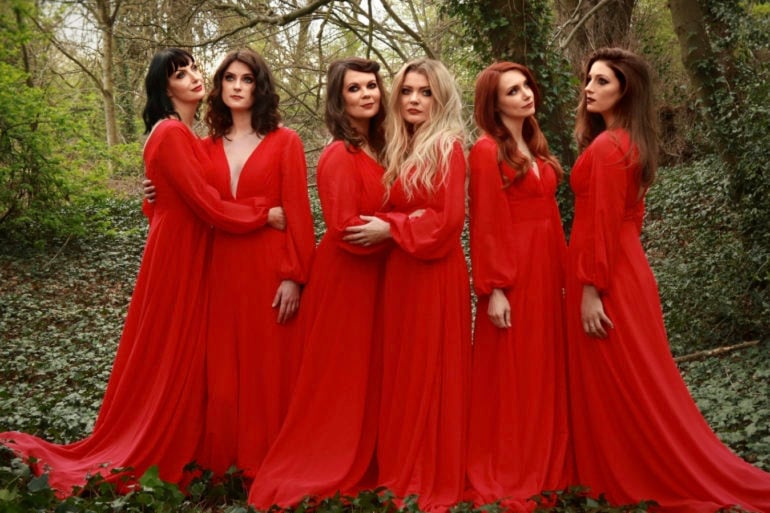 The Mediaeval Baebes standing in the woods, all dressed in long red dresses