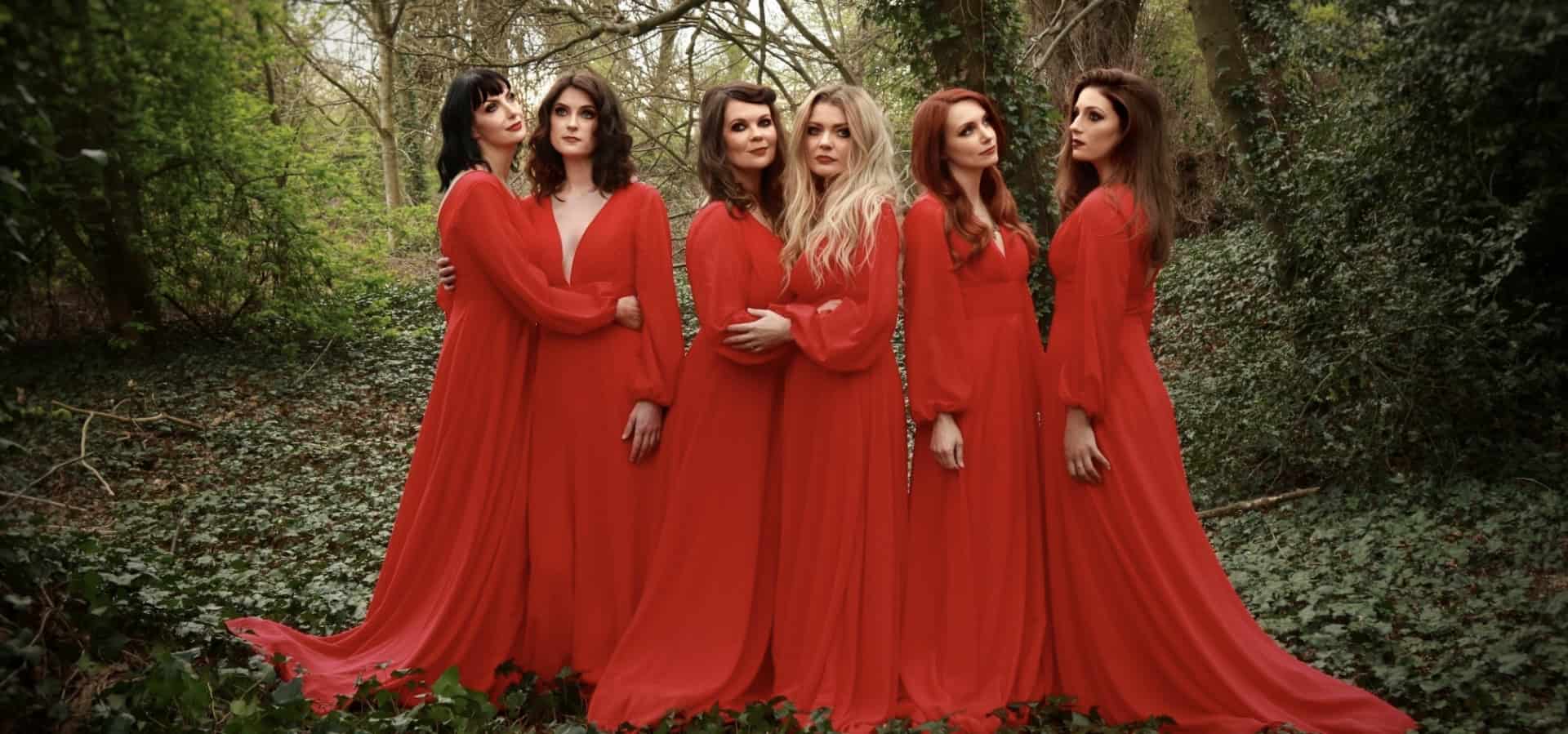 The Mediaeval Baebes standing in the woods, all dressed in long red dresses