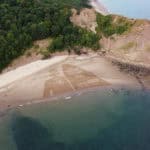 Aerial view of sand art - showing person with gas mask holding a surfboard with the word 'the ocean needs you'