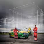 Ambulance staff in front of a car and helicopter and sketch outline on top of airbase