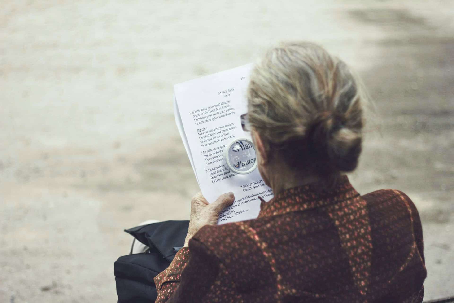 Older woman reading a French poetry book using a magnifying glass