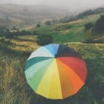 Person sitting in the countryside with a colour umbrella