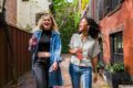 Two young women walking down a street holding glass bottles of pop