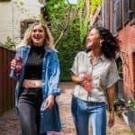 Two young women walking down a street holding glass bottles of pop