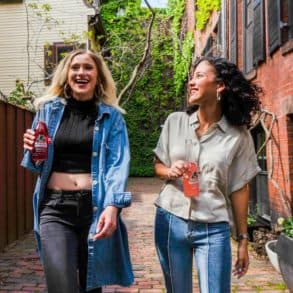 Two young women walking down a street holding glass bottles of pop