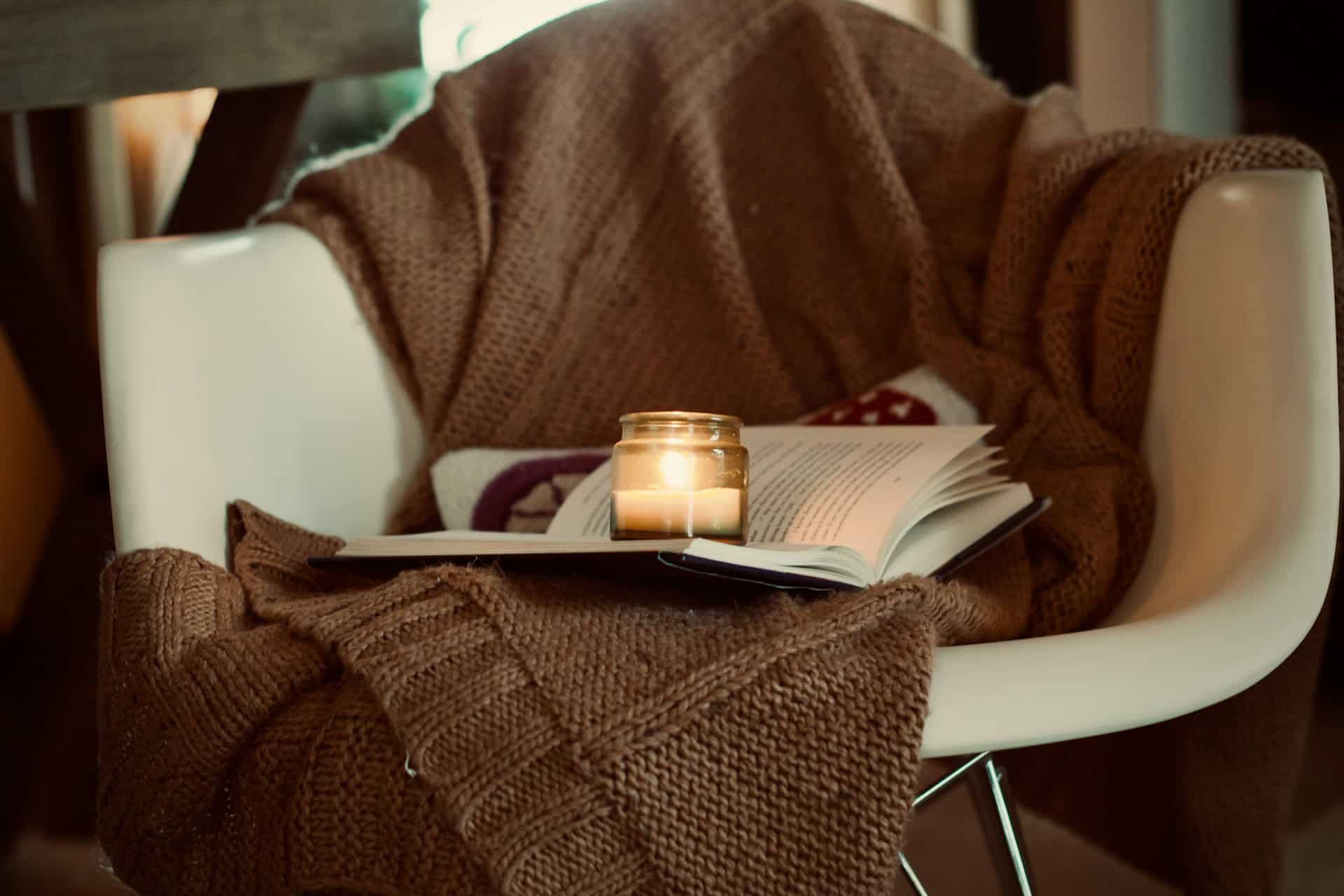 blanket draped over a chair with a book and lit candle on the chair