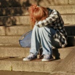 teenager sat on steps in front of building with head in hands