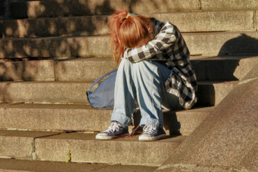 teenager sat on steps in front of building with head in hands