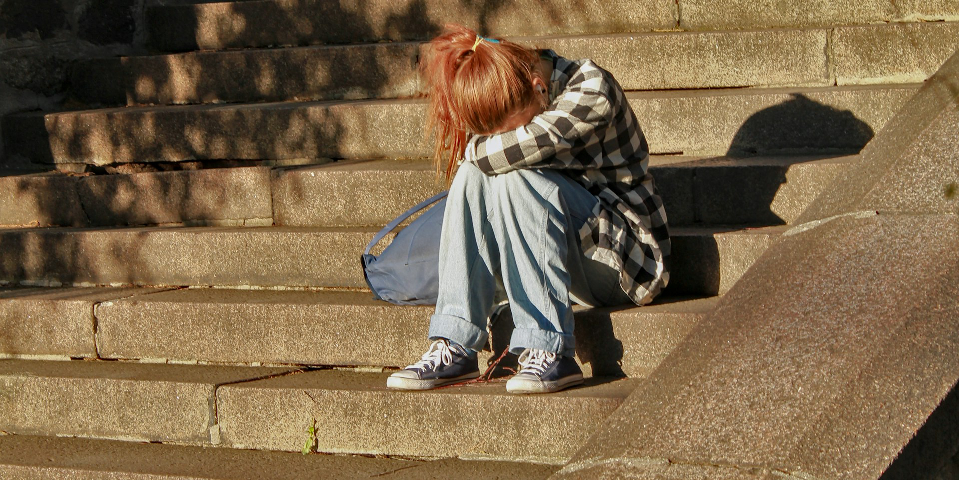 teenager sat on steps in front of building with head in hands