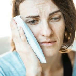 woman with toothache holding a cold compress to her cheek