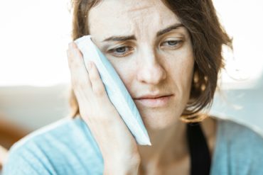 woman with toothache holding a cold compress to her cheek