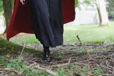 ground shot of woman in boots and long cape walking through grounds of appuldurcombe