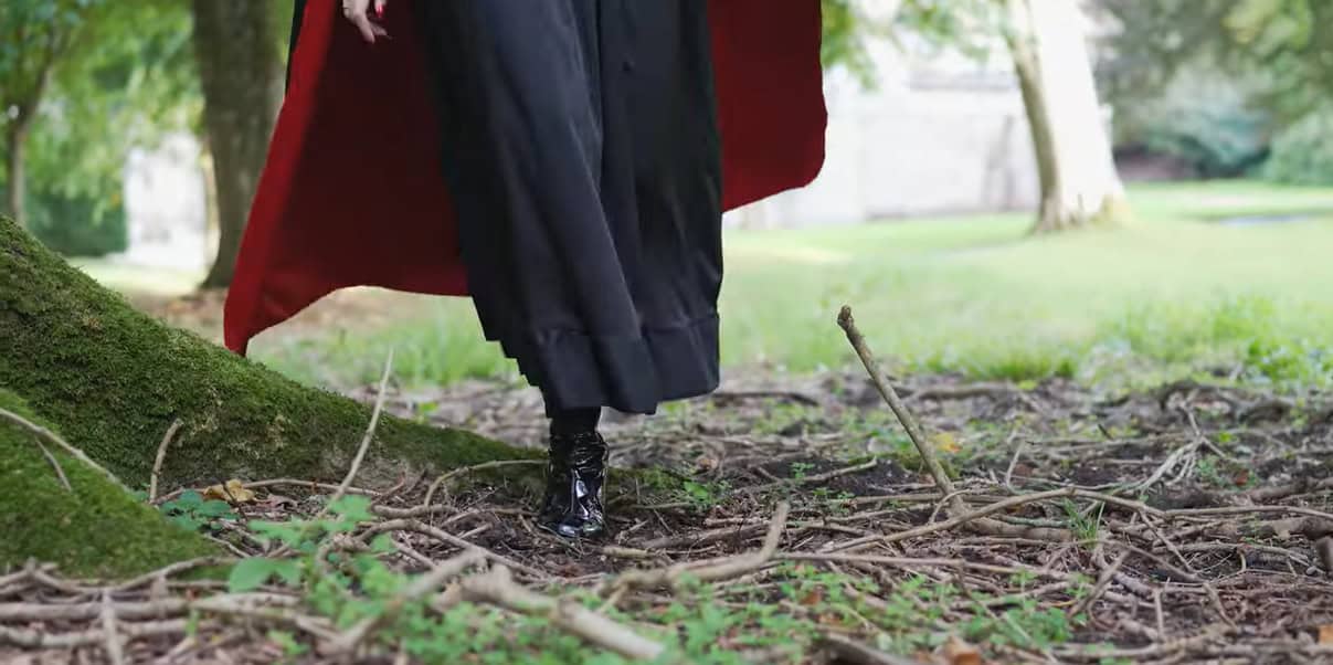 ground shot of woman in boots and long cape walking through grounds of appuldurcombe