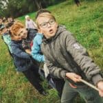 children playing tug of war in a field by the edge of woodland