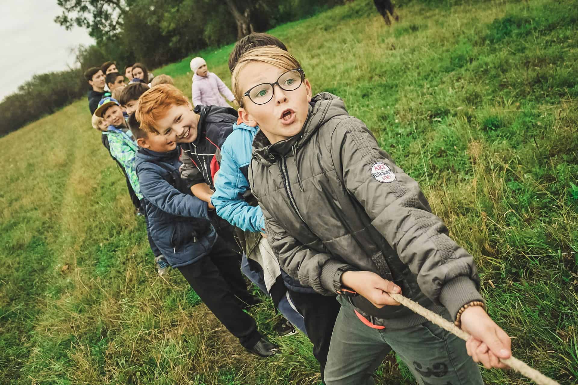 children playing tug of war in a field by the edge of woodland