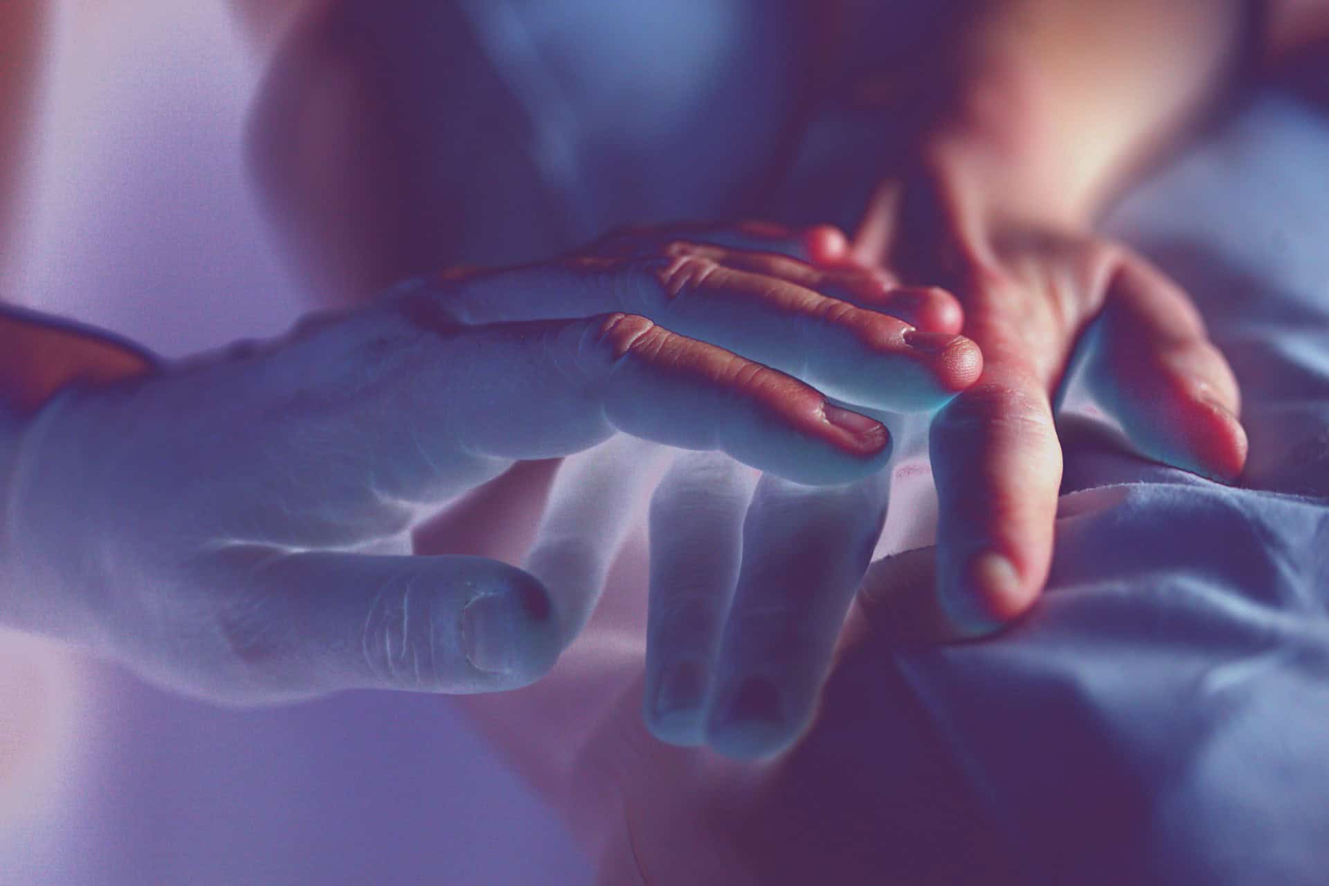 person holding the hand of another in a hospital bed