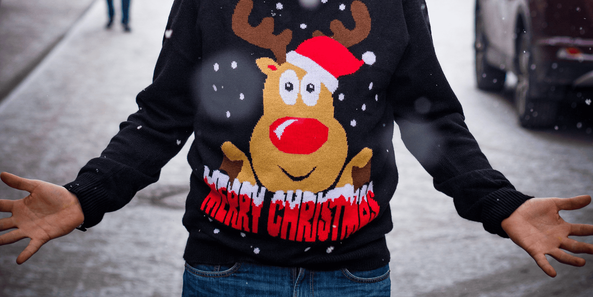 Man wearing a christmas jumper standing on the street in the snow