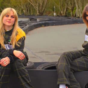 Lily and Lottie from The Pill sitting in jumpsuits at the karting track