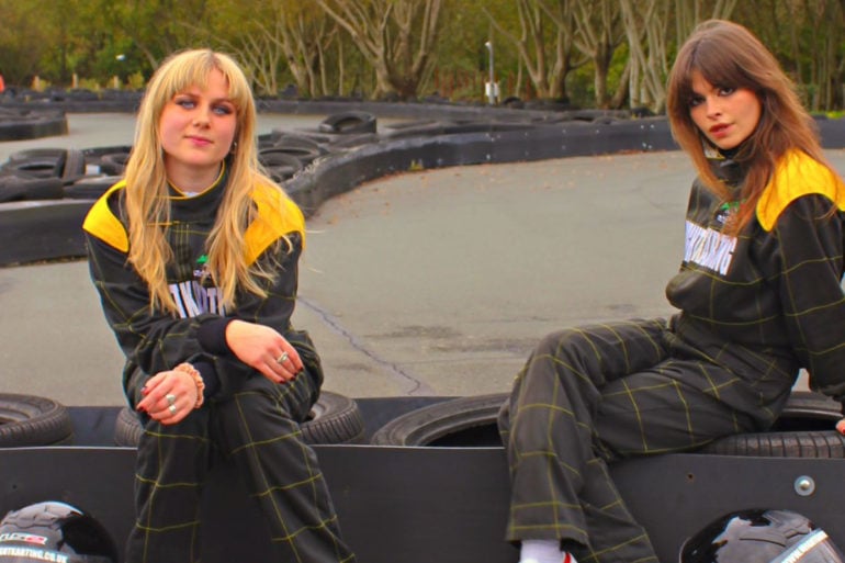 Lily and Lottie from The Pill sitting in jumpsuits at the karting track