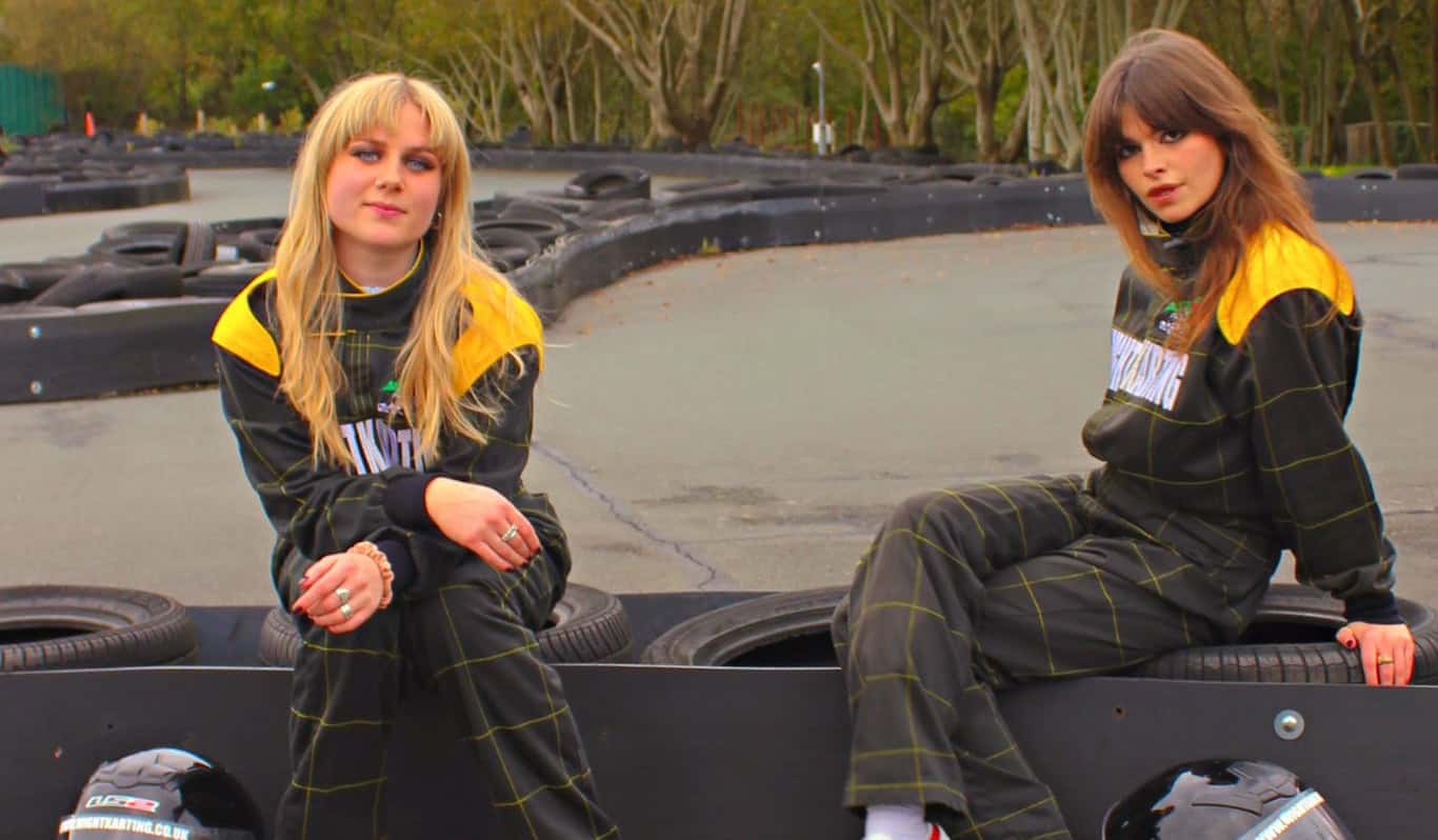 Lily and Lottie from The Pill sitting in jumpsuits at the karting track