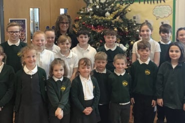 Pupils and teacher standing in front of Christmas tree at aWootton primary school