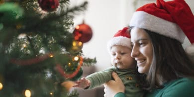 woman and baby looking at a christmas tree, both wearing santa hats