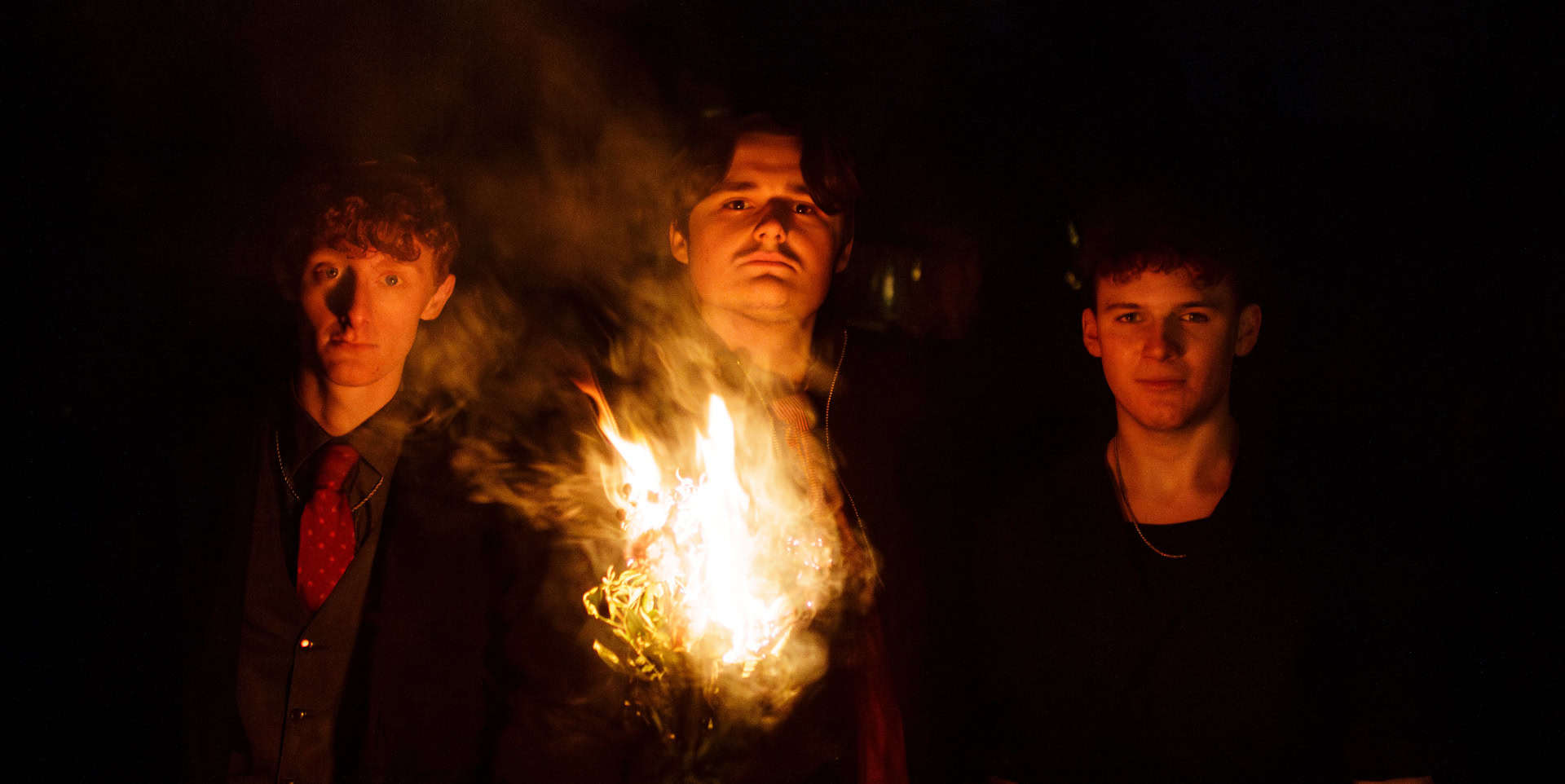 Three band members of 5 degrees north standing in the darkness holding a burning torch