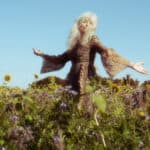 Smiling blissed out woman enjoying nature in a field of wild flowers, with blue sky behind her