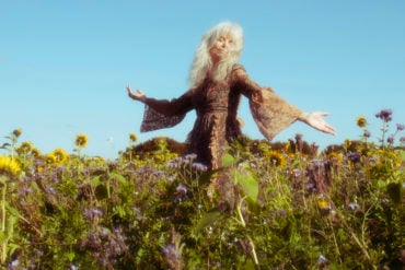 Smiling blissed out woman enjoying nature in a field of wild flowers, with blue sky behind her