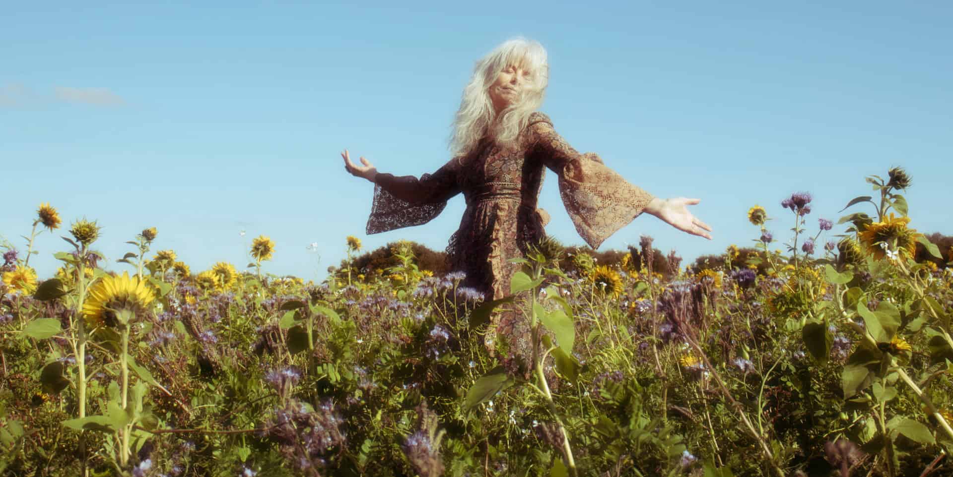 Smiling blissed out woman enjoying nature in a field of wild flowers, with blue sky behind her