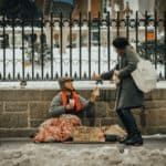 Homeless man sitting on the street and talking to a passerby