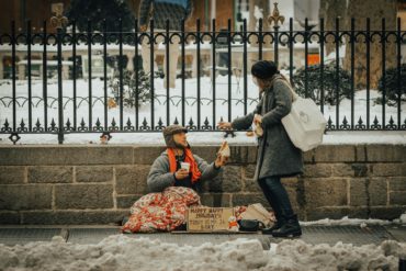 Homeless man sitting on the street and talking to a passerby