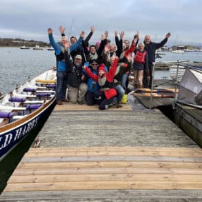 Old Harry wooden gig in the water with the Rowing crew on the pontoon