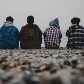 four teenagers sitting on a beach wit their backs to the camera