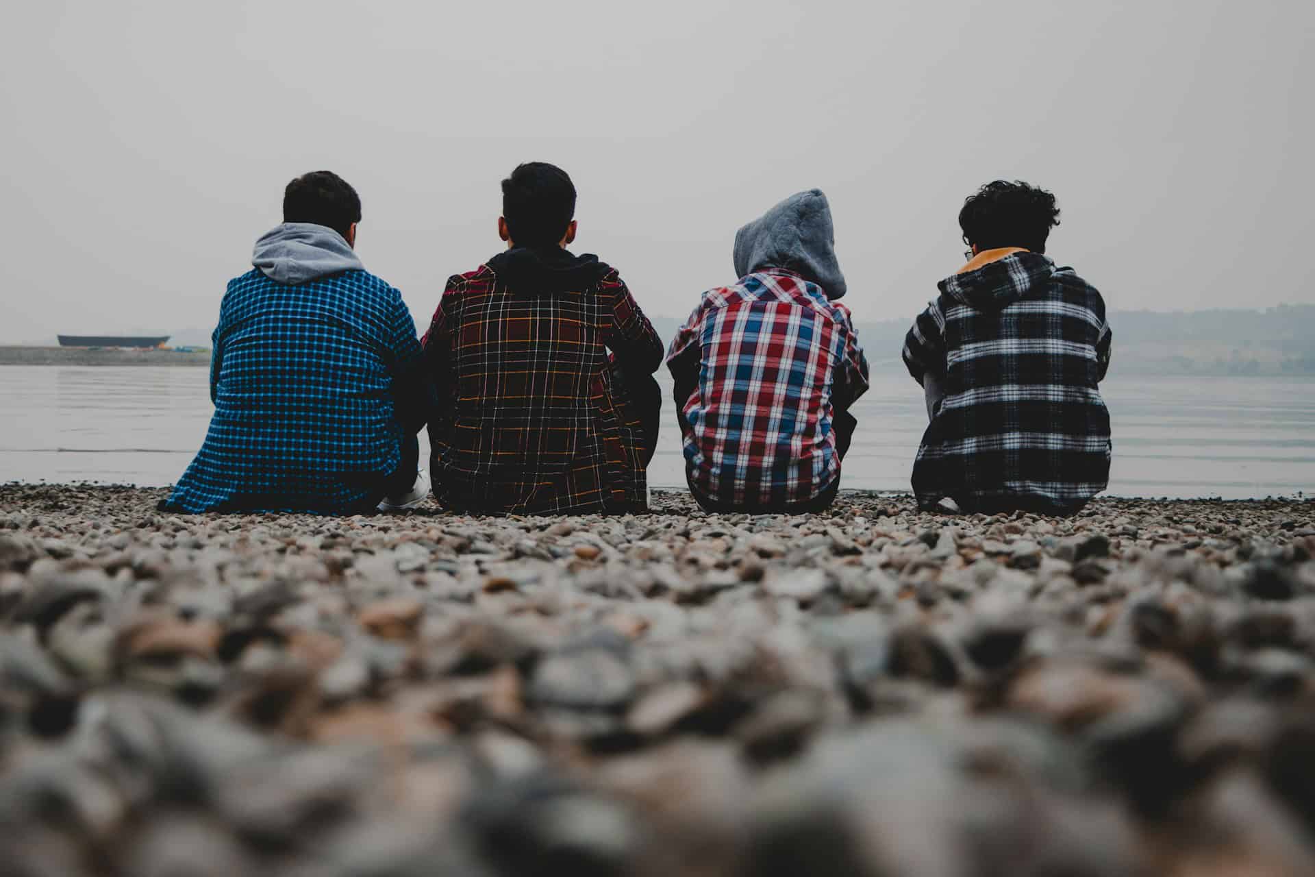 four teenagers sitting on a beach wit their backs to the camera