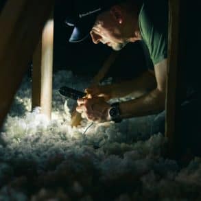 man in attic cutting electrical cables among insulation