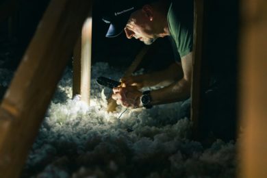 man in attic cutting electrical cables among insulation