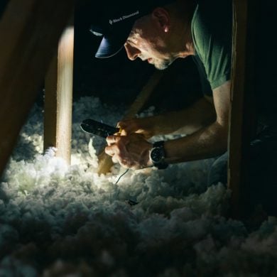 man in attic cutting electrical cables among insulation