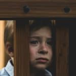 unhappy sad child looking through wood slats of play equipment