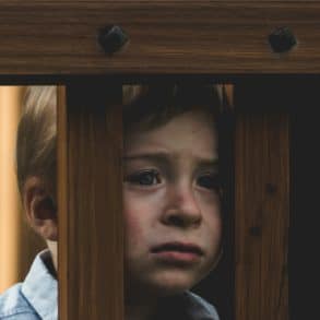 unhappy sad child looking through wood slats of play equipment