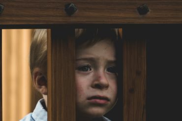 unhappy sad child looking through wood slats of play equipment