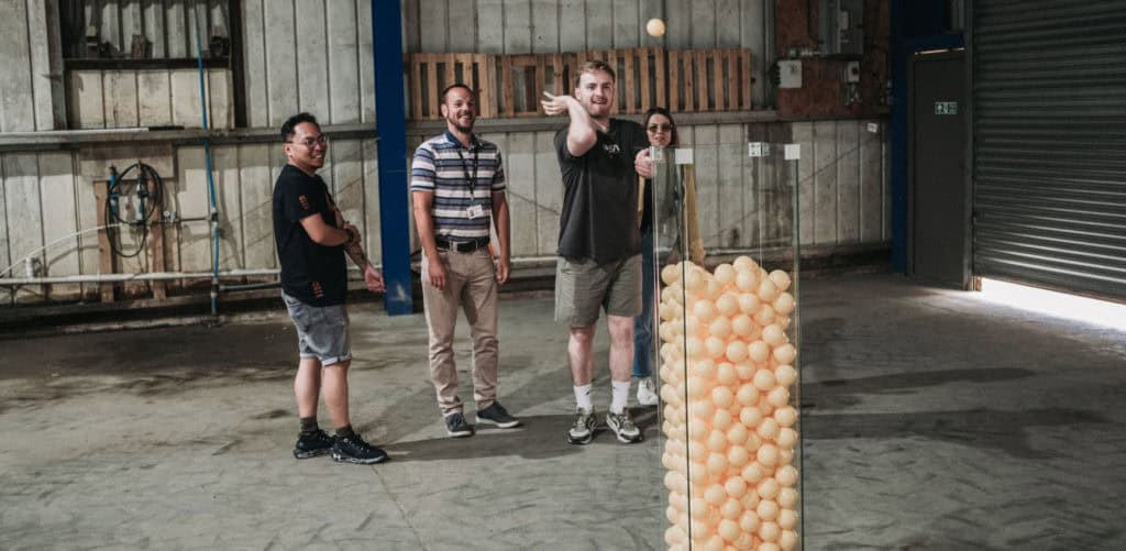 Three people trying to through balls into a large clear container