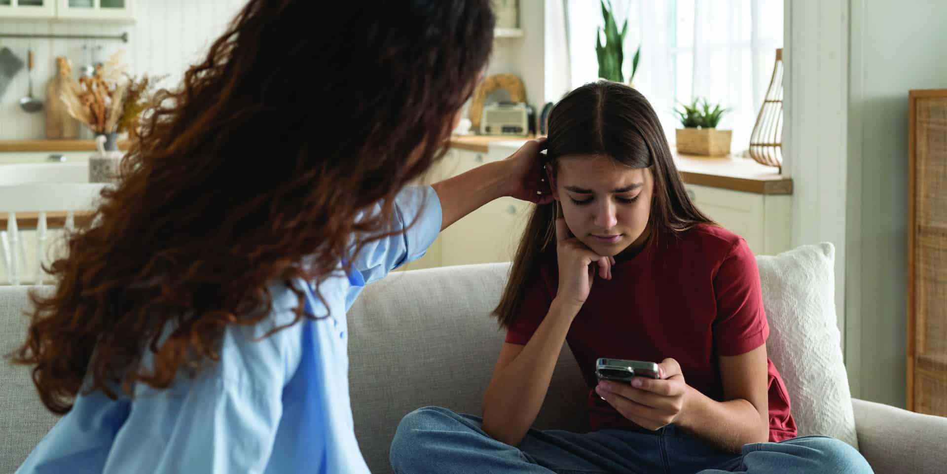 Supportive mother comforting sad teenage girl rejected by friends, helping depressed teen daughter to deal with breakup. Upset depressed adolescent child looking at phone at home, waiting for call